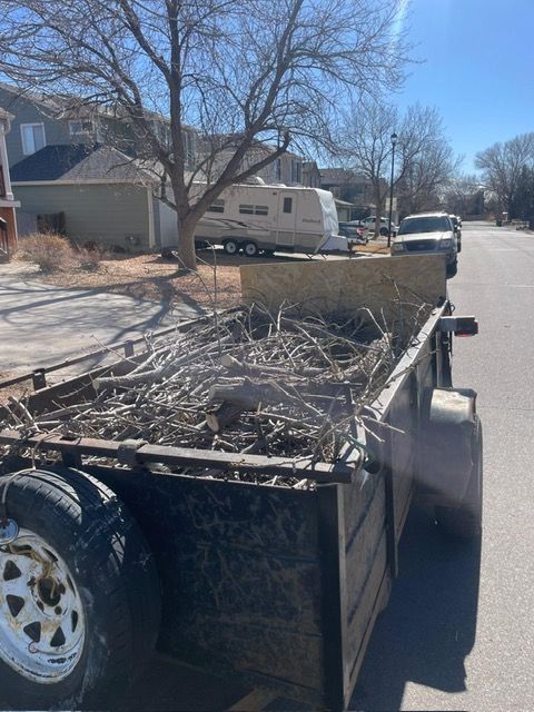 Trailer filled with yard debris parked on a sunny suburban street near houses and a parked van