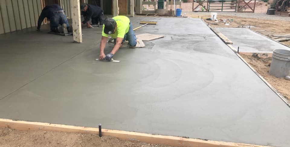 Worker smoothing wet concrete on a newly poured driveway beside a house