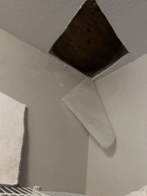 Damaged ceiling corner with a dark hole and a loose white panel hanging down