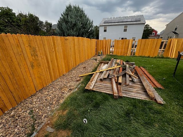 Backyard with orange fence and a pile of wooden boards on the grass and gravel path