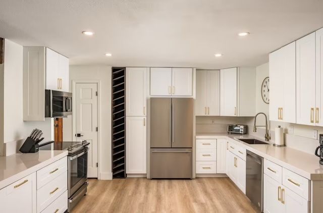 Modern white kitchen with stainless steel appliances, light wood floor, and recessed ceiling lights