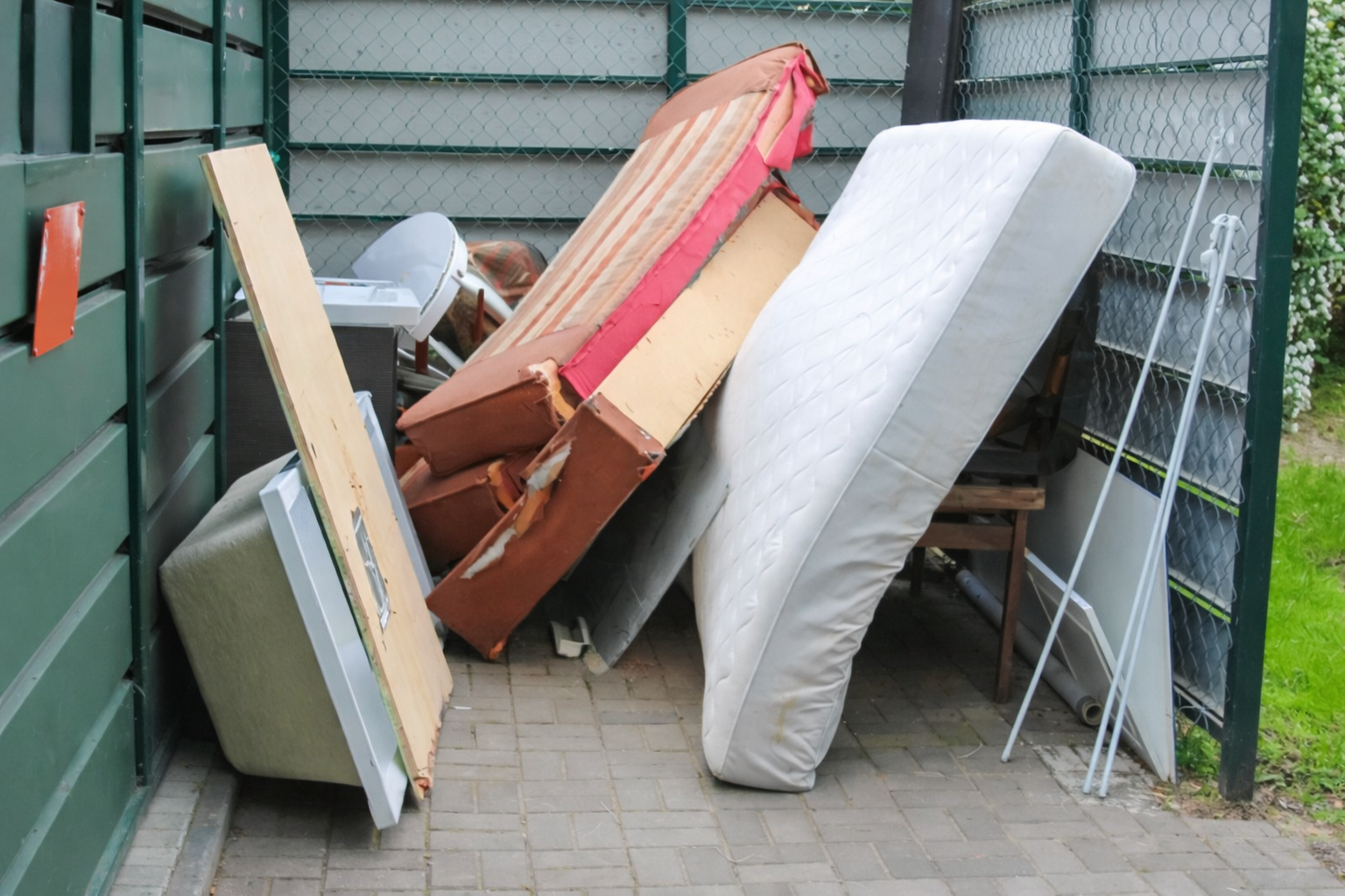 An orange excavator lifts a heavy debris-filled grapple during a building demolition near trees and a parked vehicle.