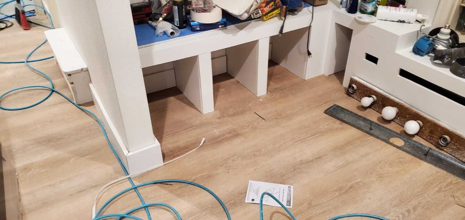 Construction site showing a white built-in shelving unit with open compartments installed over light-colored wood flooring.