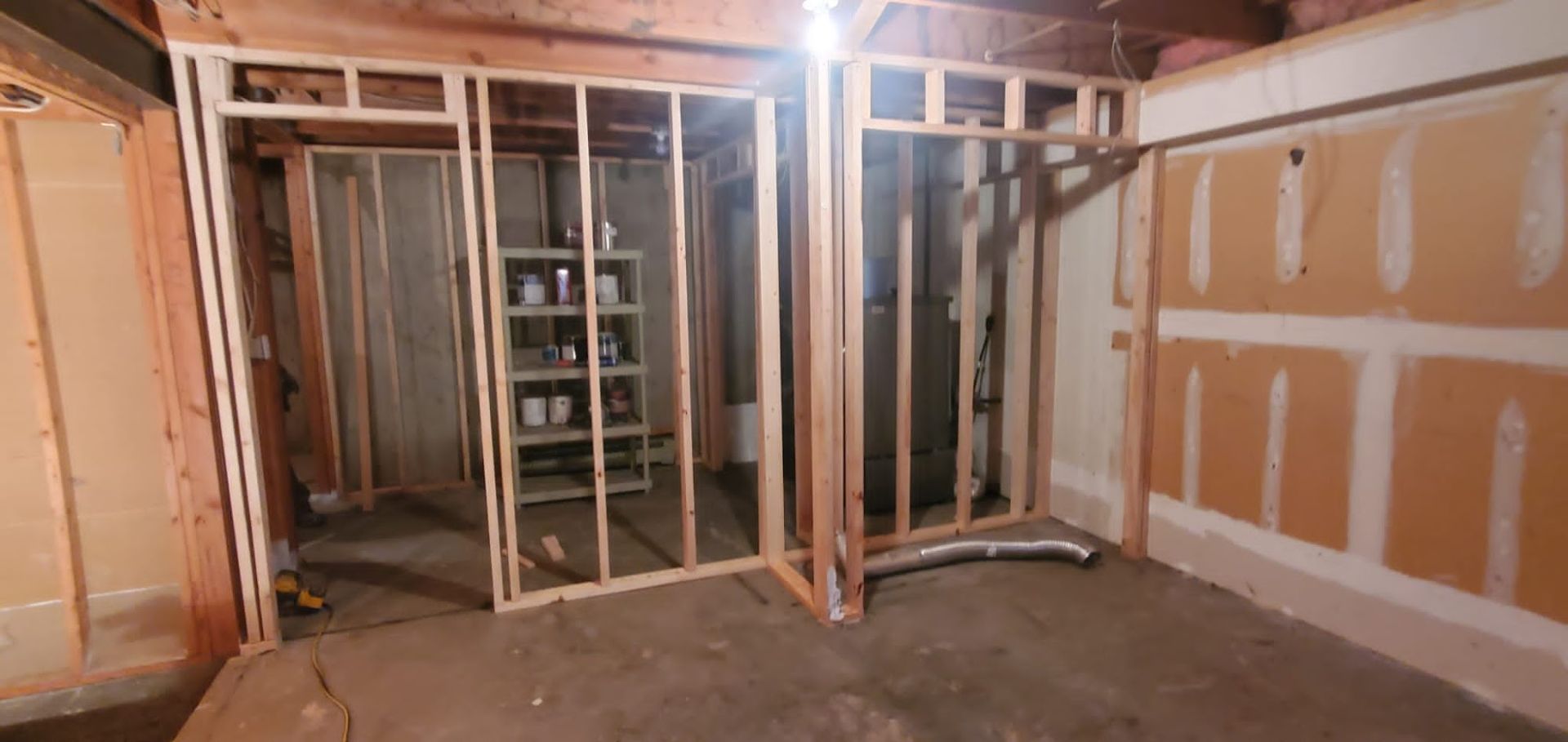 Unfinished basement construction showing wooden stud wall framing and drywall panels around a utility area.