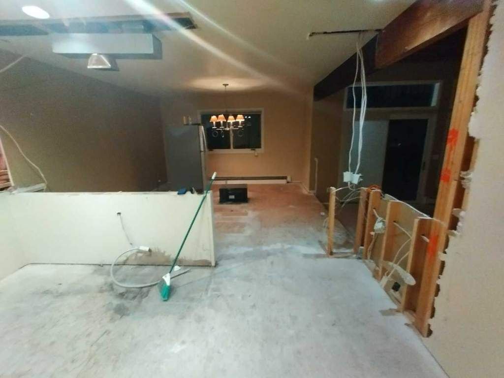 A room under renovation with bare concrete floors, an exposed wooden support beam, and partially demolished partition walls.