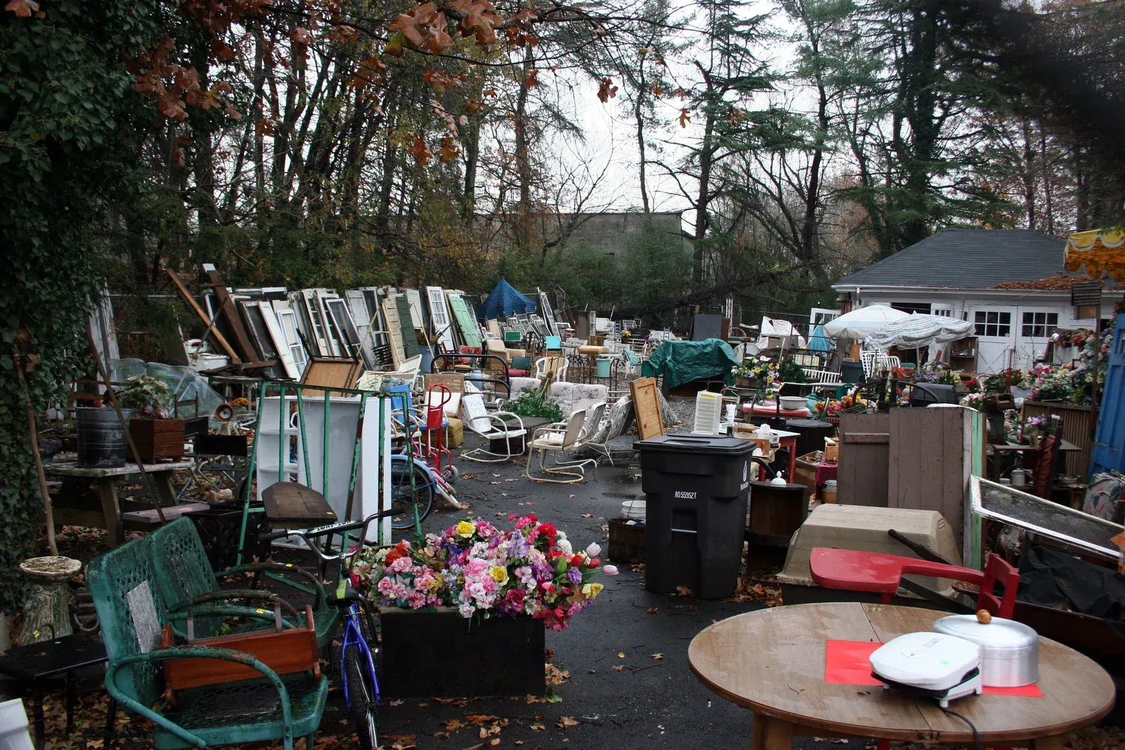 An outdoor yard sale with furniture, household goods, and various items cluttered across a driveway near a house.