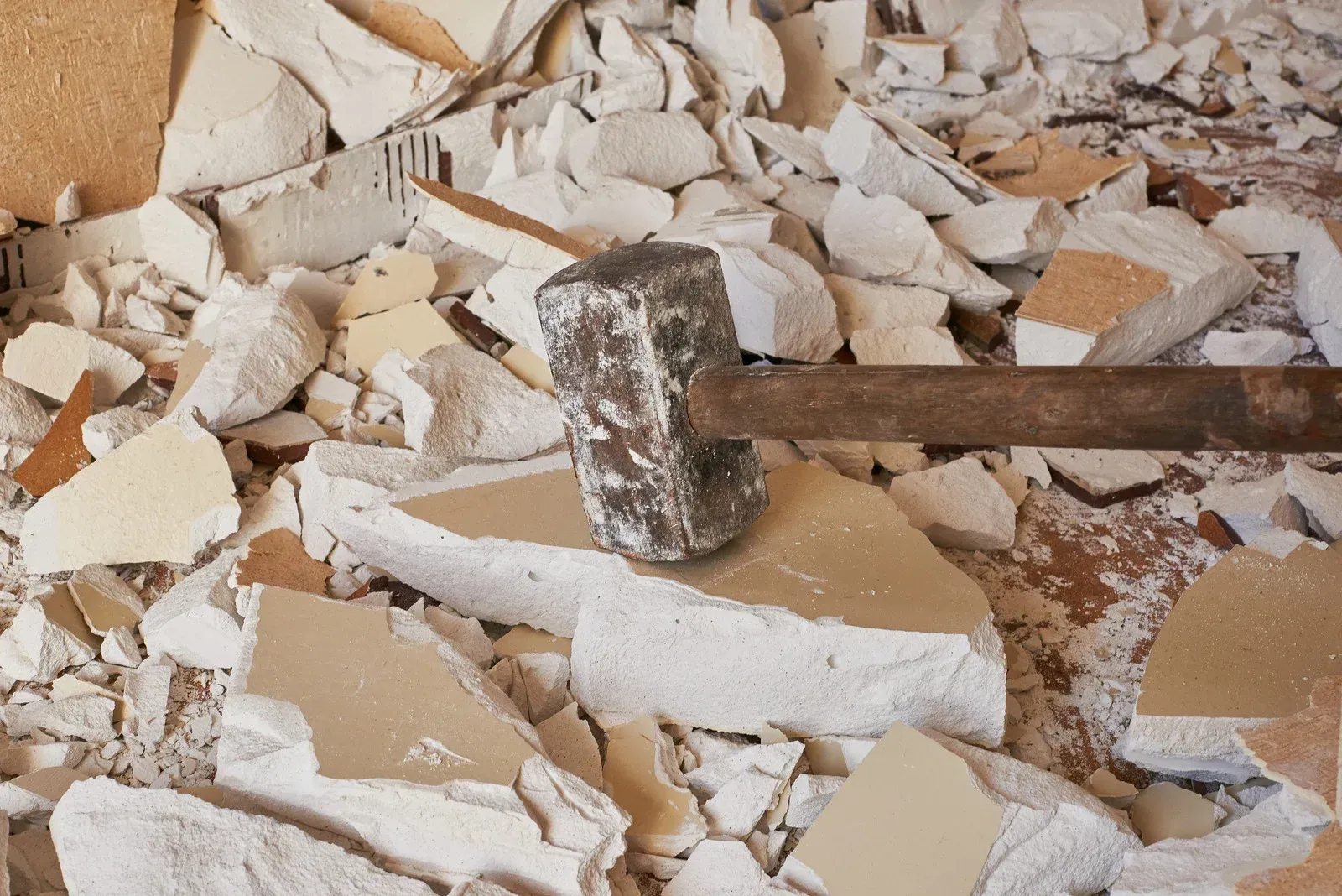 A heavy sledgehammer rests on a pile of broken drywall and plaster debris on a floor.