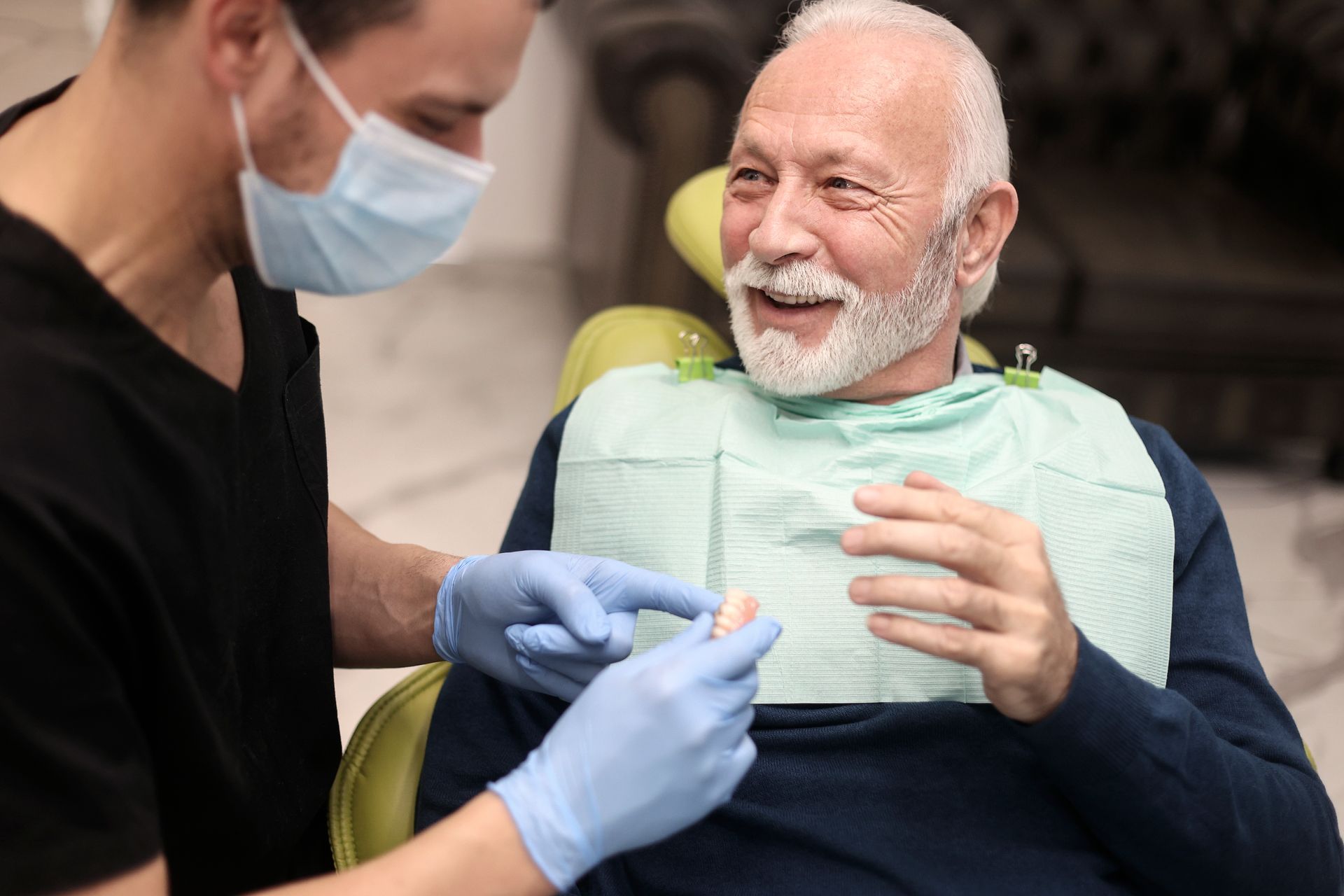Senior man at a dentist's office, looking at dentures while the doctor provides information.