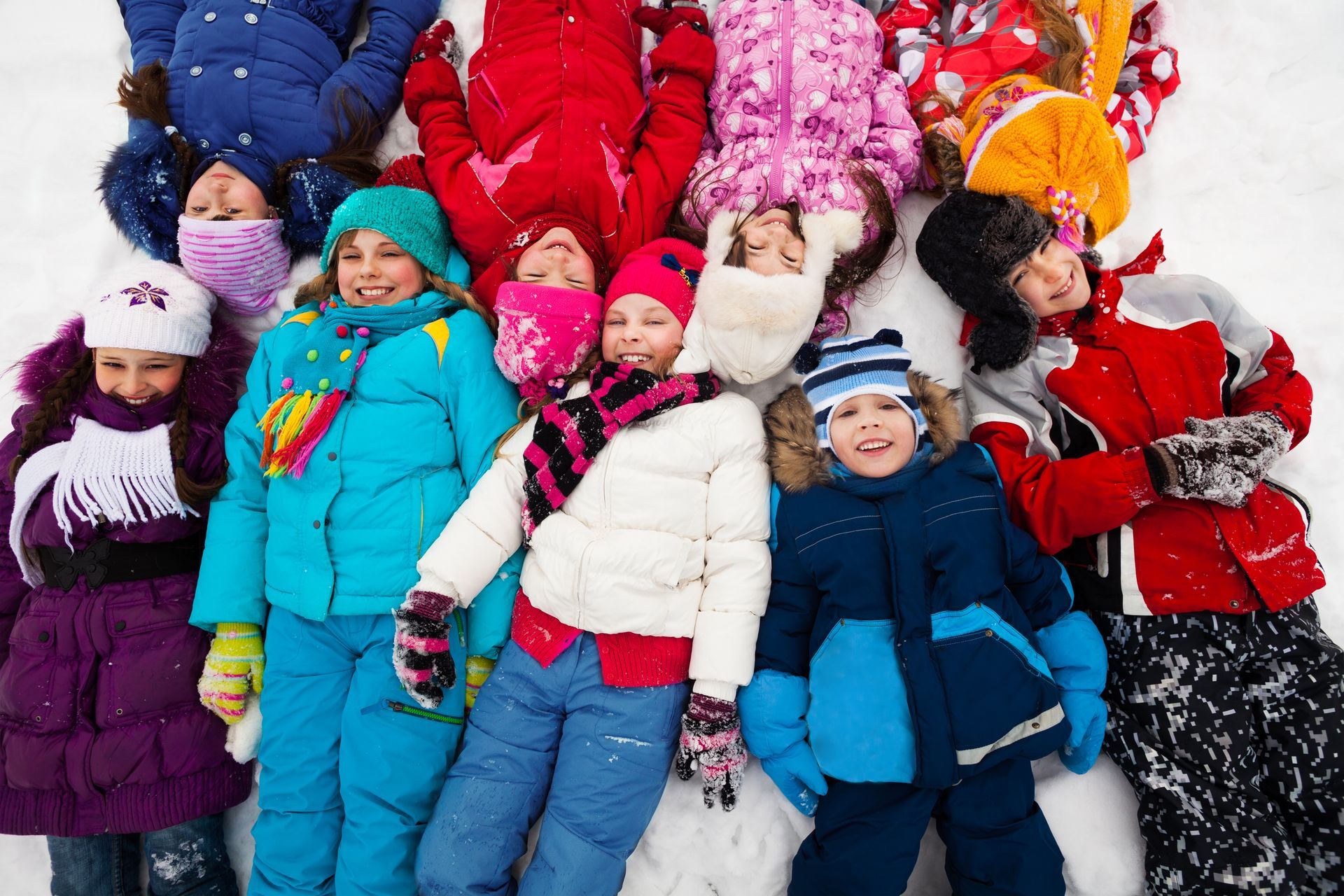 A group of children in warm clothing laying in the snow together