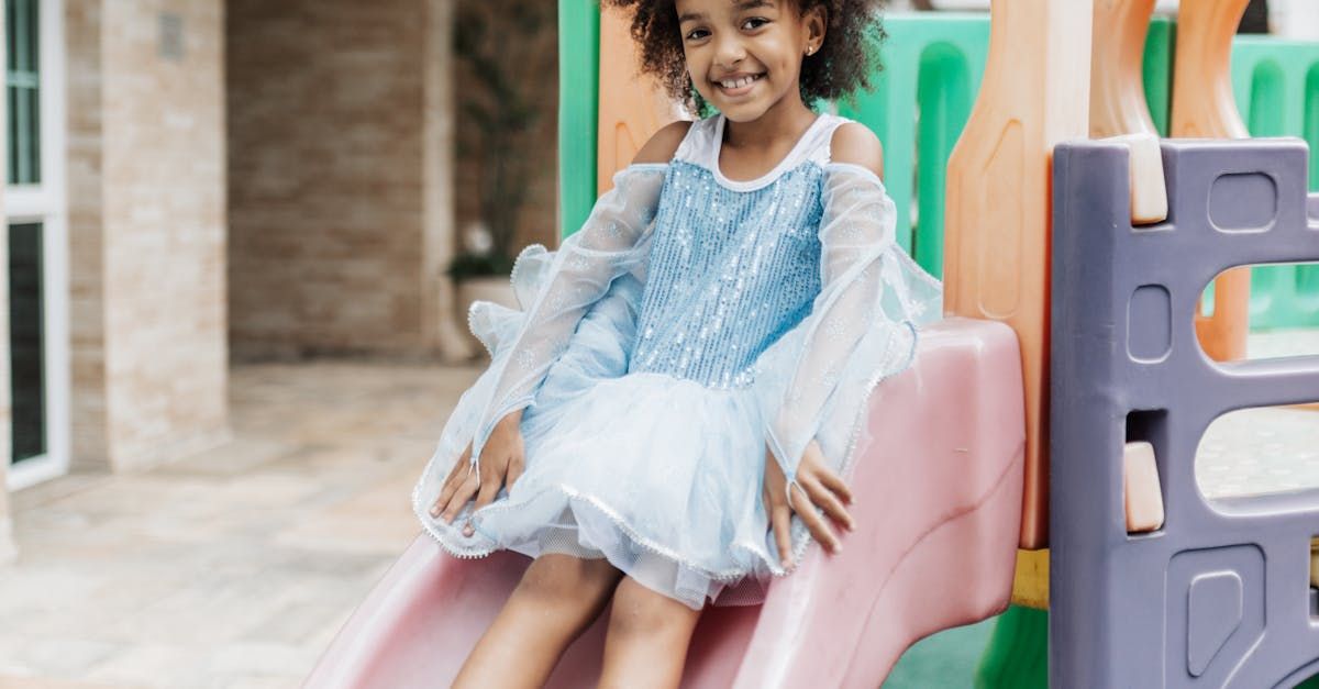 Girl in blue dress smiling while sliding down a colorful playground slide.