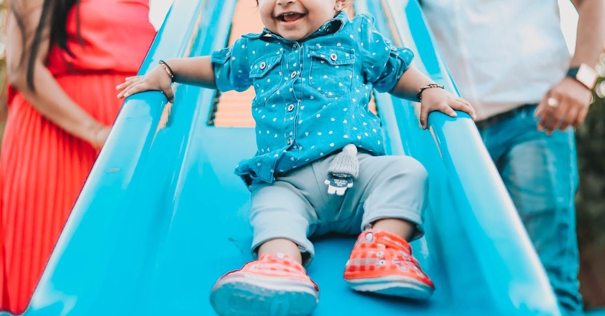 Happy child sliding down a blue slide, smiling. Parents in the background.