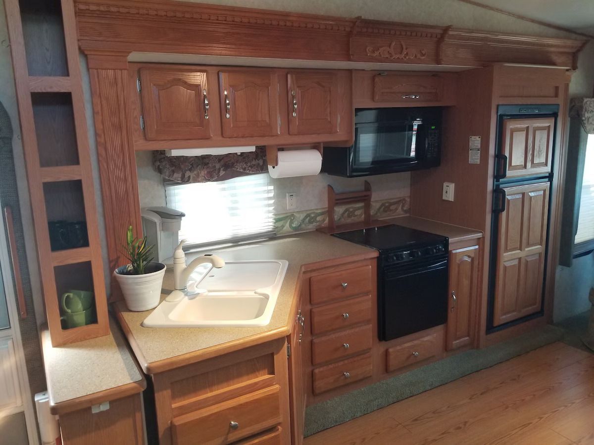 A kitchen in a rv with a sink , stove , microwave and refrigerator.
