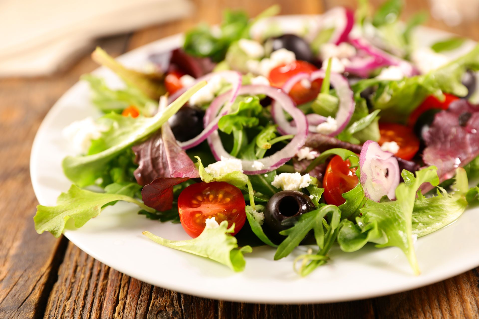 A close up of a salad on a white plate on a wooden table.