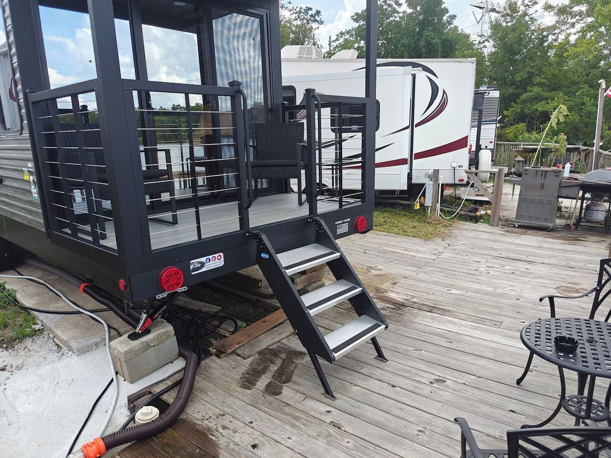 A trailer with stairs leading up to it is parked on a wooden deck.