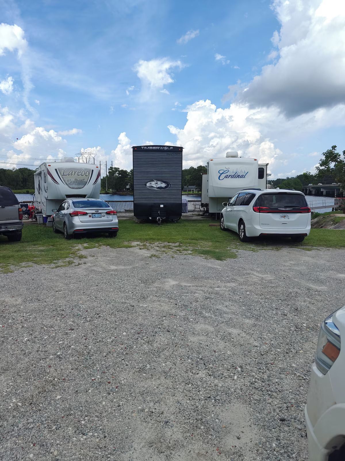 A lot of cars and rvs are parked in a gravel lot.