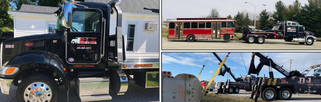 A black tow truck tows various vehicles, including a bus and equipment, on a sunny day.