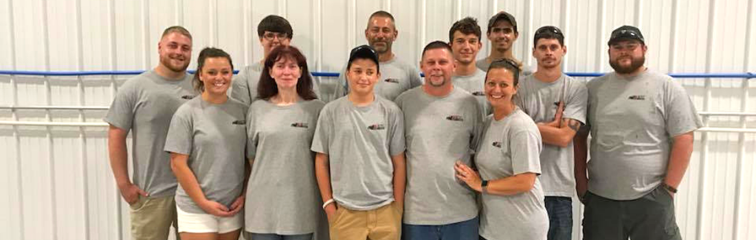 Group of people wearing matching gray shirts posing in front of a white wall.