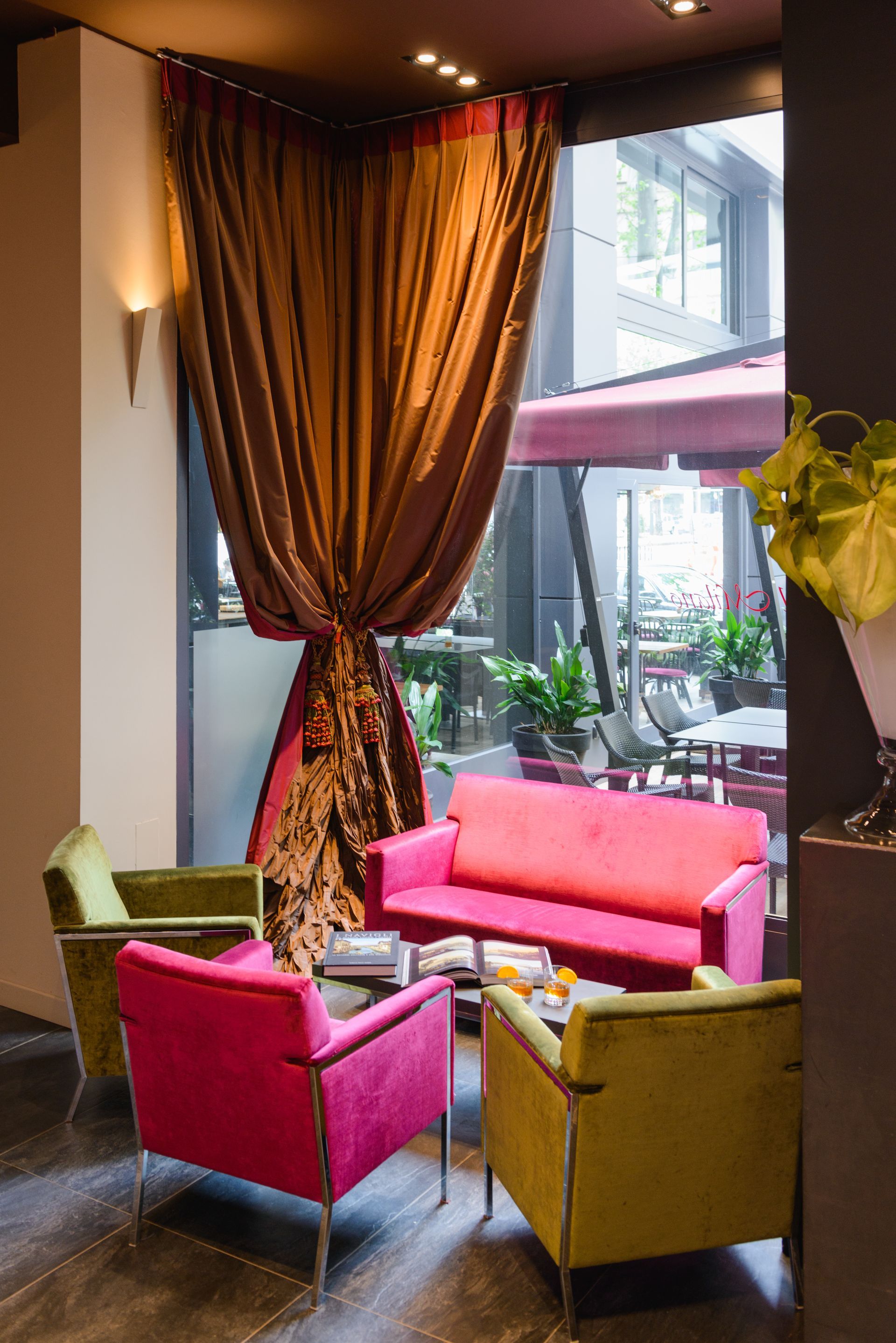 Acogedor salón con sillas rosas, amarillas y verdes junto a una gran ventana y cortinas rojas.