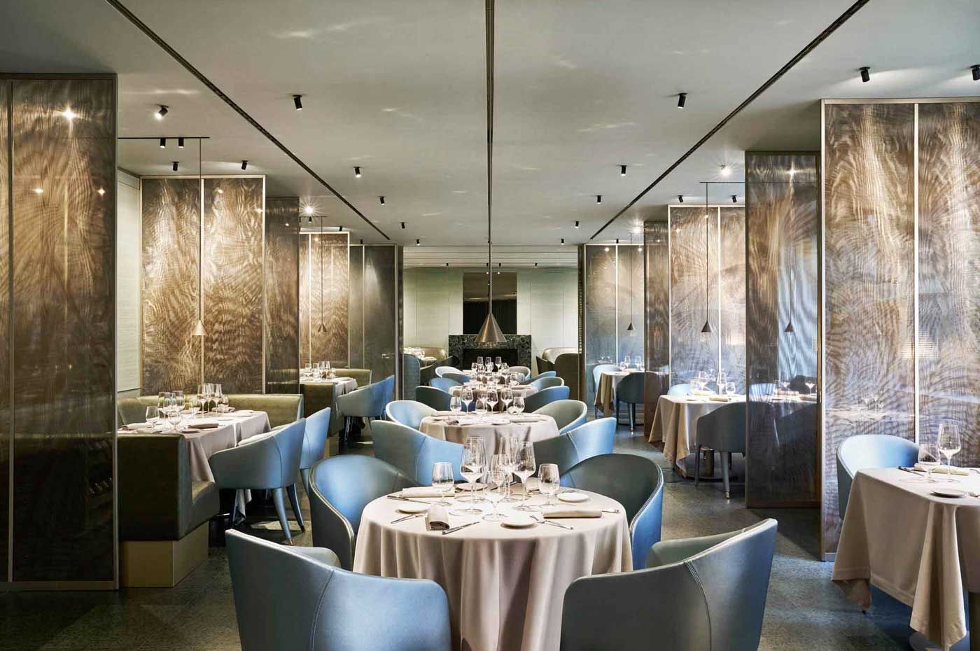 Elegante sala da pranzo del ristorante con tavoli rotondi, sedie blu e pannelli a specchio alle pareti.
