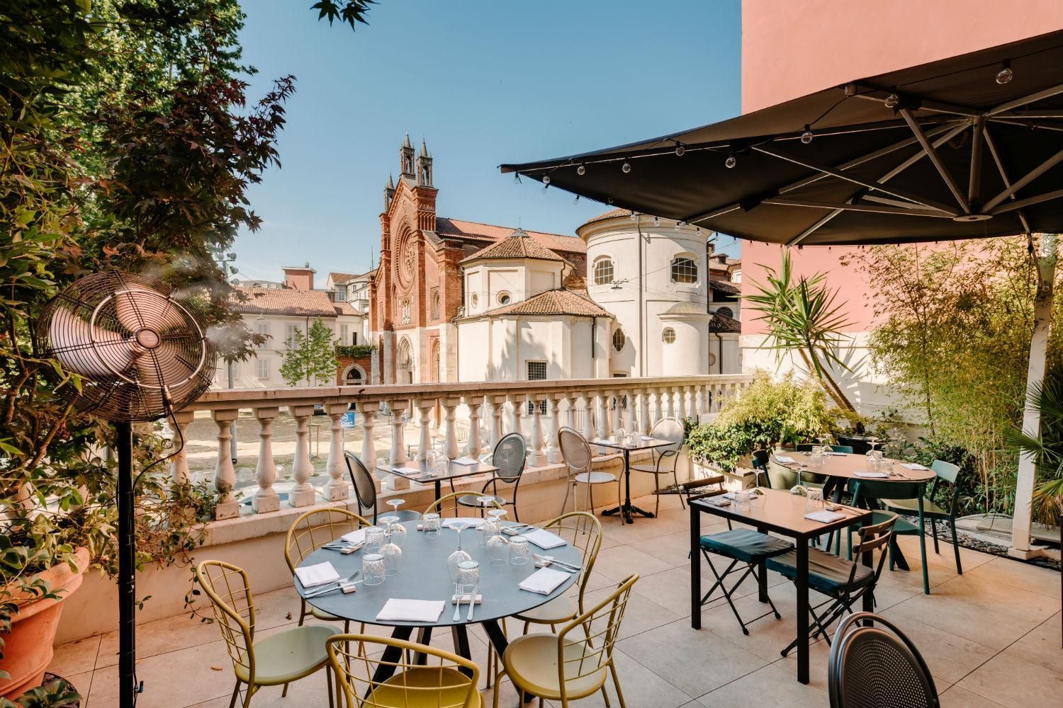 Terrazza soleggiata con tavolini, ombrelloni e, al di là di una balaustra in pietra, la vista sui palazzi della città.