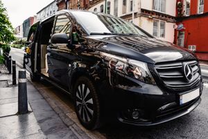 Furgone Mercedes nero parcheggiato su una strada cittadina bagnata, accanto a edifici e dissuasori.