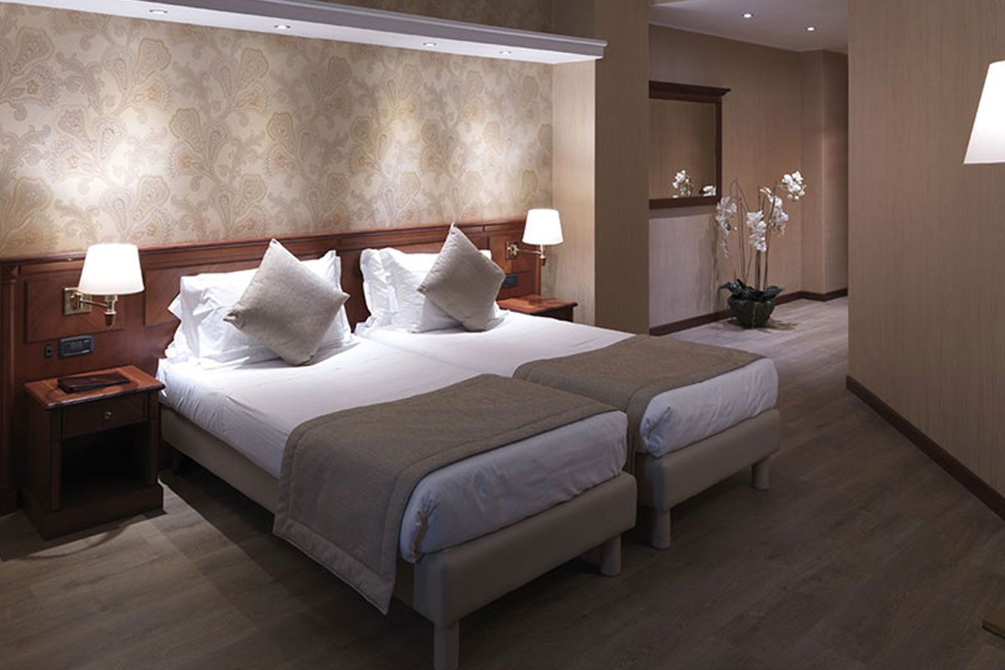 Habitación de hotel moderna con dos camas individuales, lámparas de noche y una decoración cálida en tonos neutros.