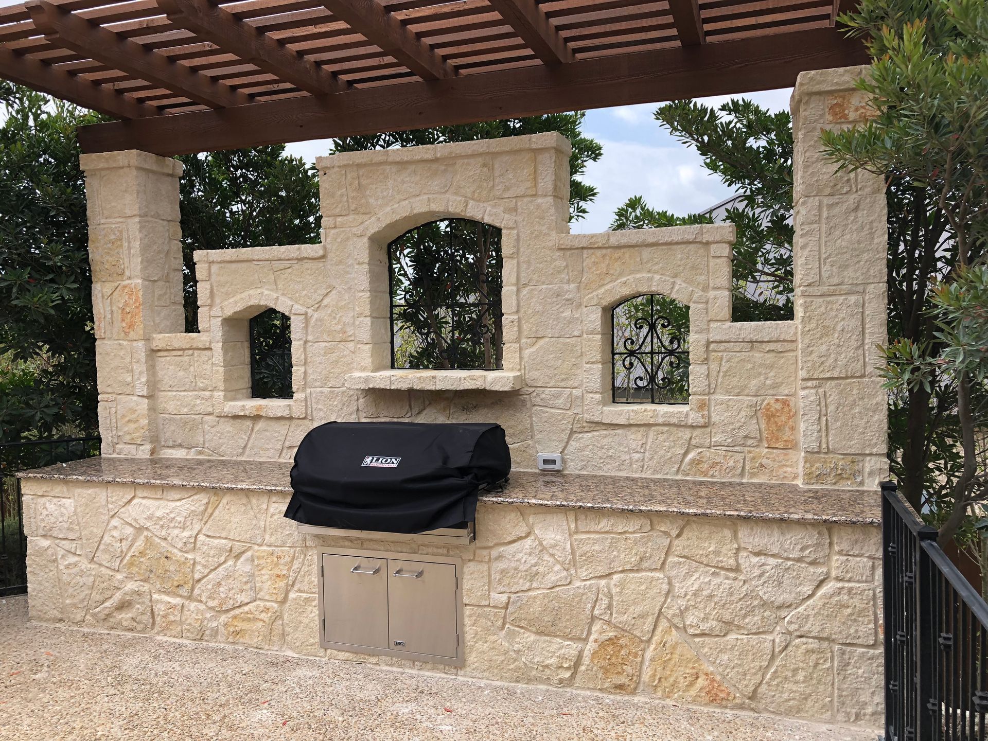 A grill with a black cover sits under a pergola built by Fine Patio Design San Antonio TX