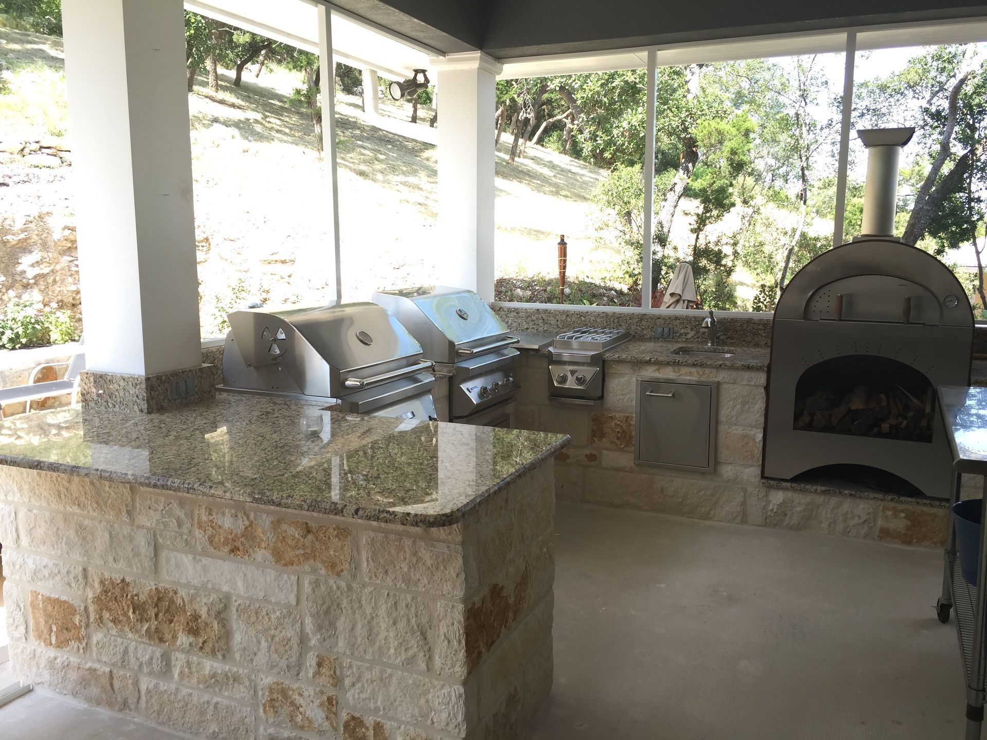 An outdoor kitchen with a grill and a pizza oven built by Fine Patio Design San Antonio TX