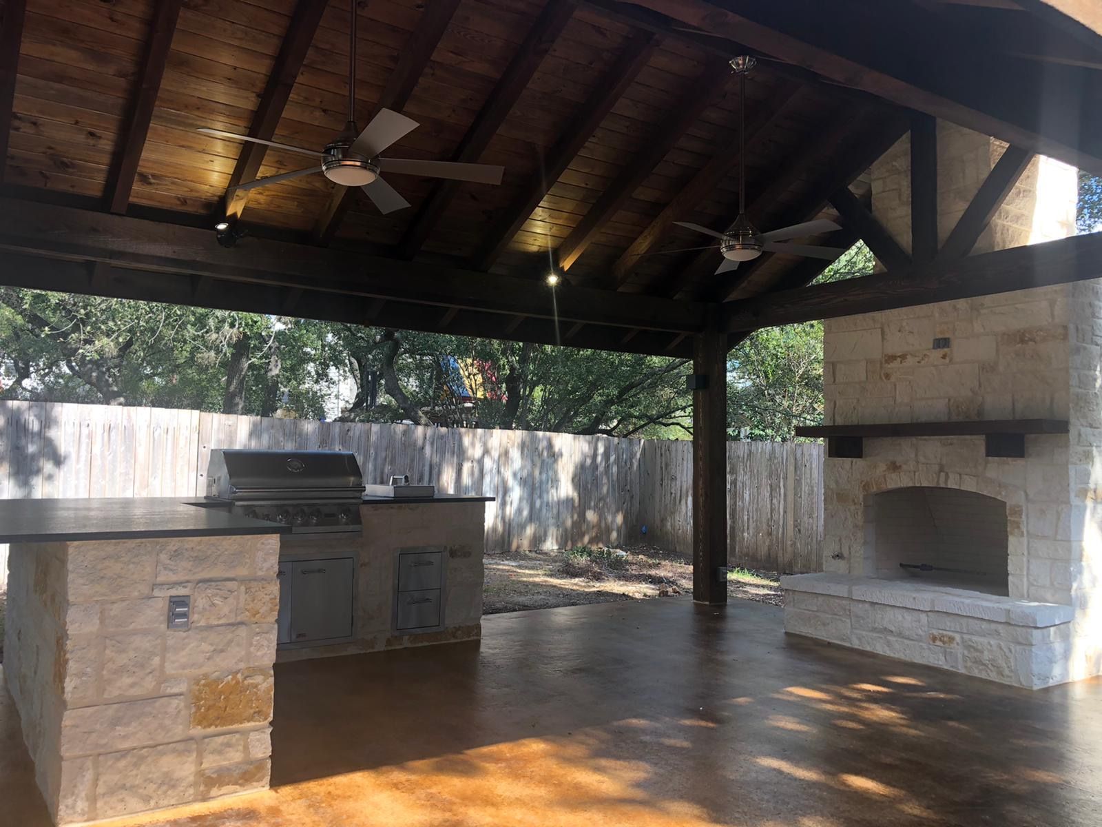 An outdoor kitchen with a ceiling fan and a fireplace built by Fine Patio Design San Antonio TX