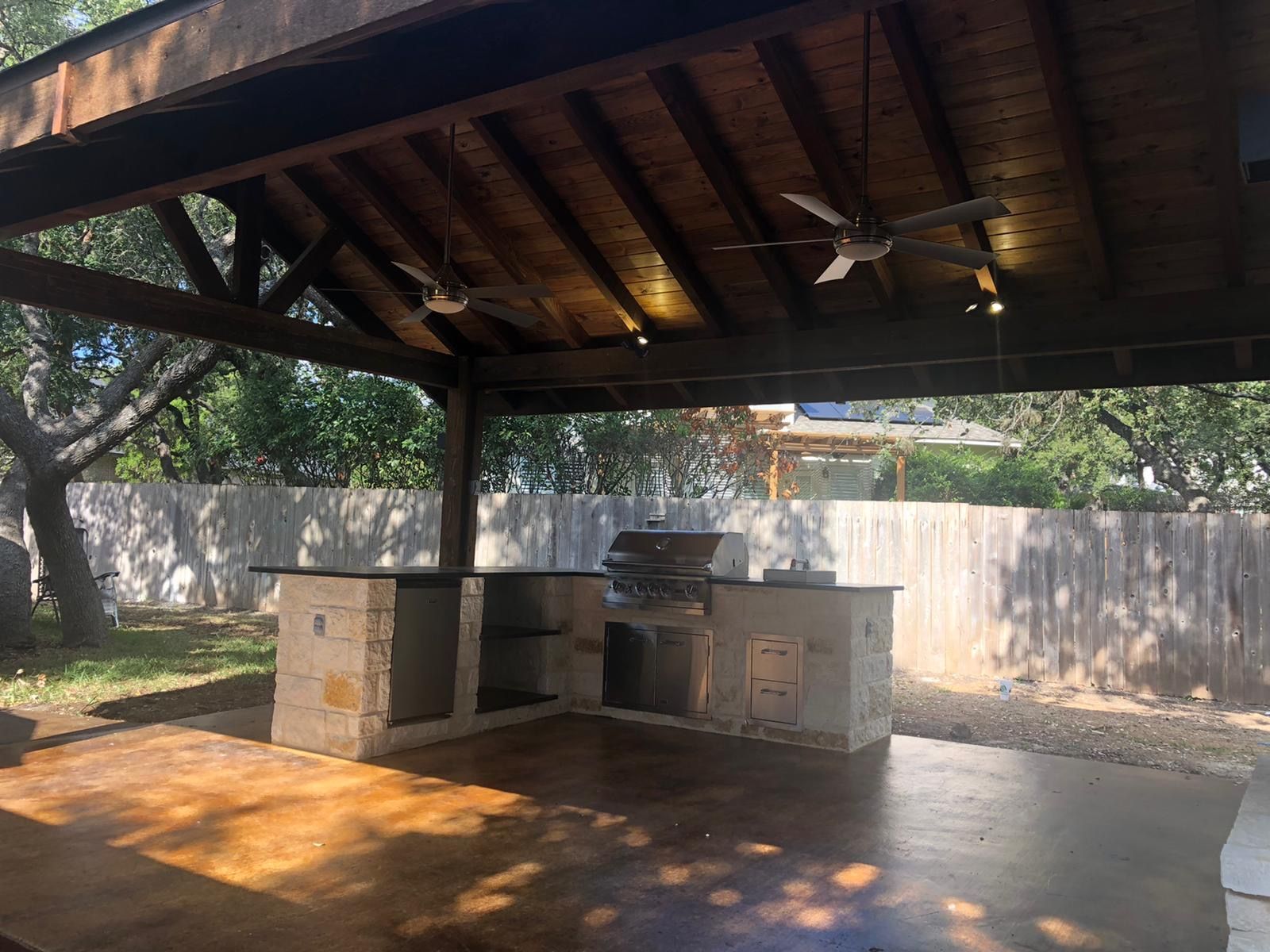An outdoor kitchen under a wooden roof with a ceiling fan built by Fine Patio Design San Antonio TX