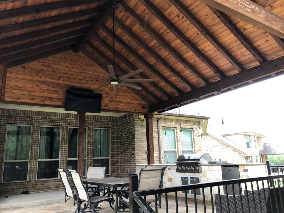 A patio with a table and chairs under a wooden roof built by Fine Patio Design San Antonio TX