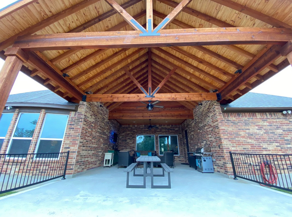 A picnic table under a wooden roof in front of a brick house built by Fine Patio Design San Antonio TX