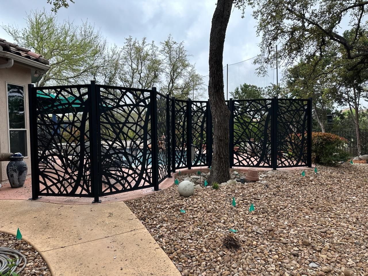 A black fence with a pattern on it is in front of a house built by Fine Patio Design San Antonio TX