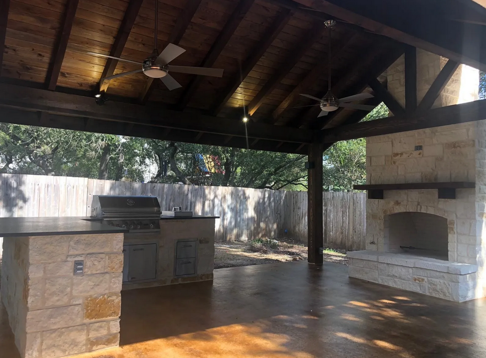 An outdoor kitchen with a ceiling fan and a fireplace built by Fine Patio Design San Antonio TX