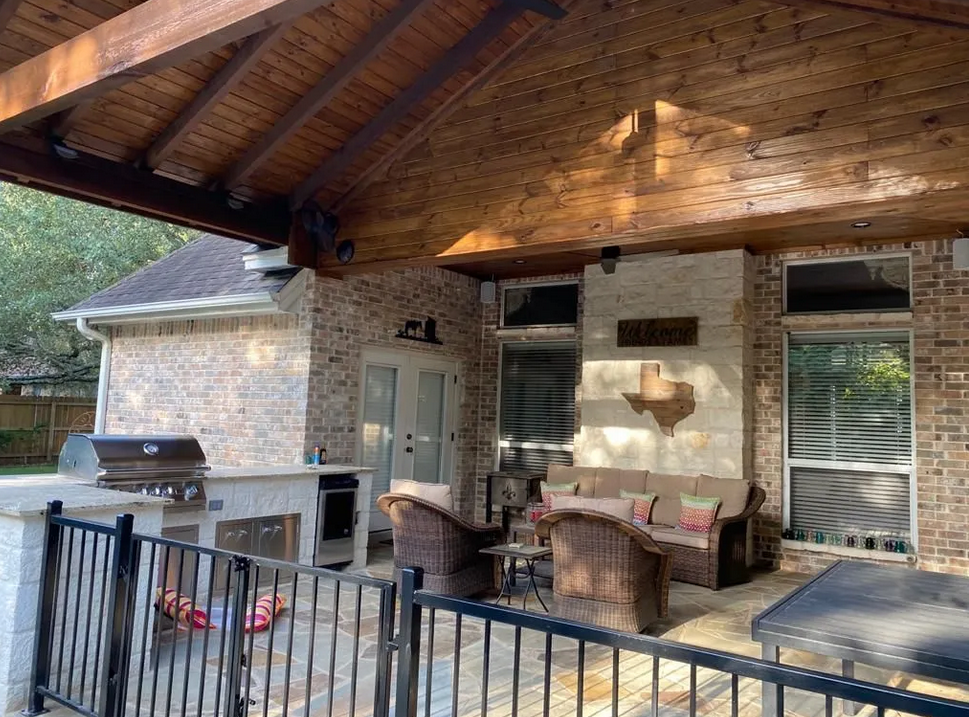 A patio with a grill and chairs under a wooden roof built by Fine Patio Design San Antonio TX