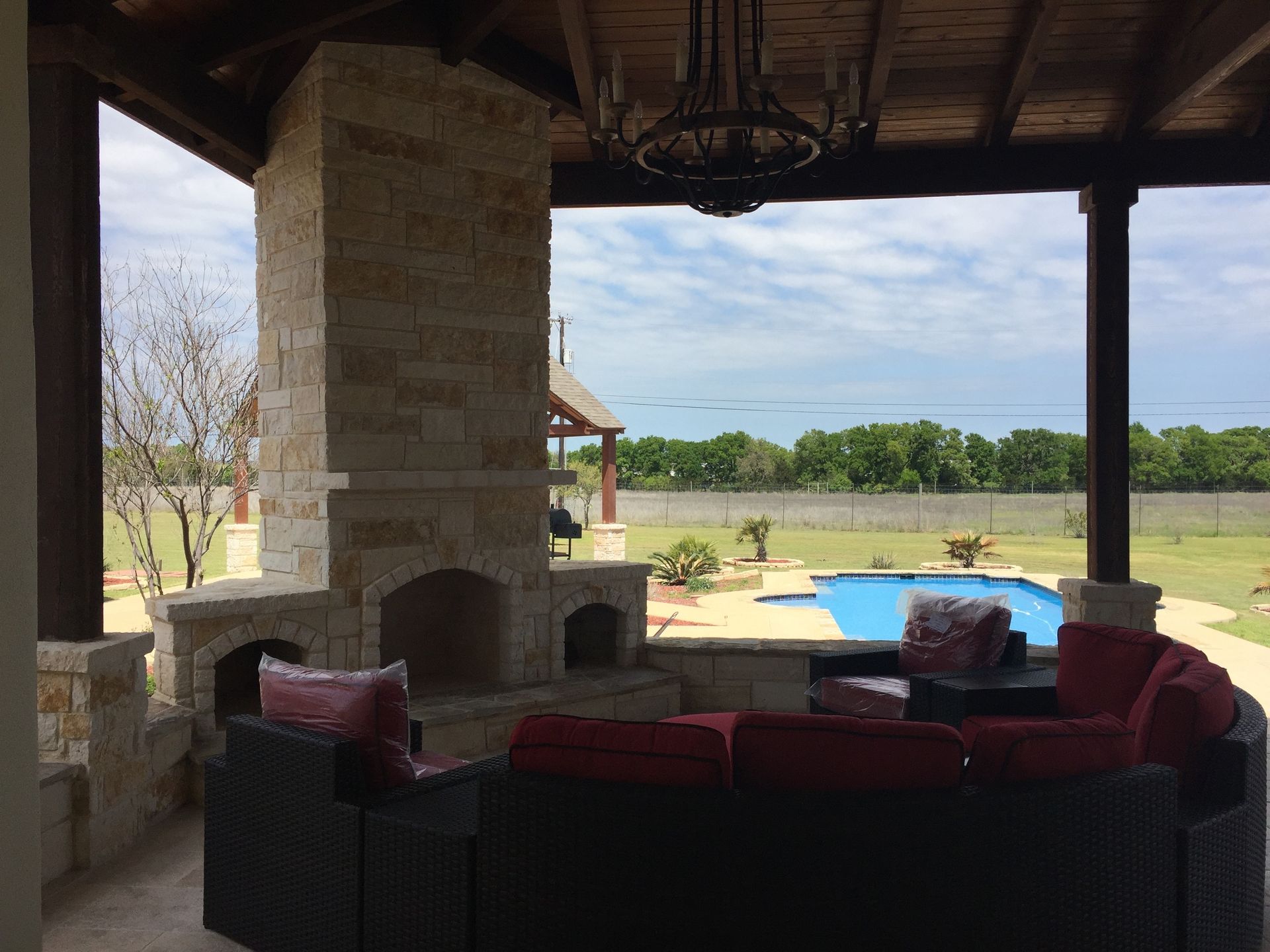 A patio with a fireplace and a pool in the background built by Fine Patio Design San Antonio TX