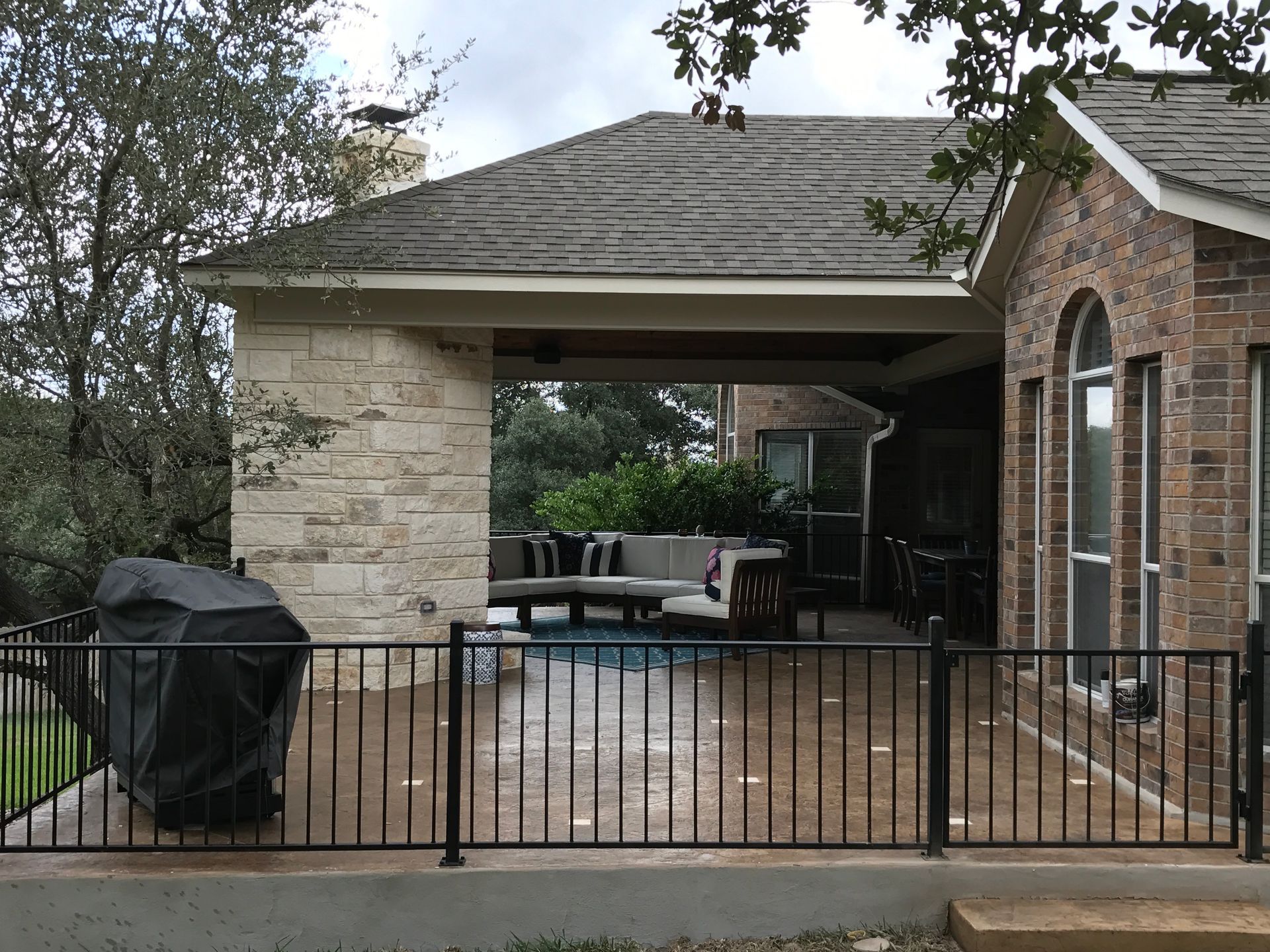 A brick house with a patio area behind a metal fence built by Fine Patio Design San Antonio TX