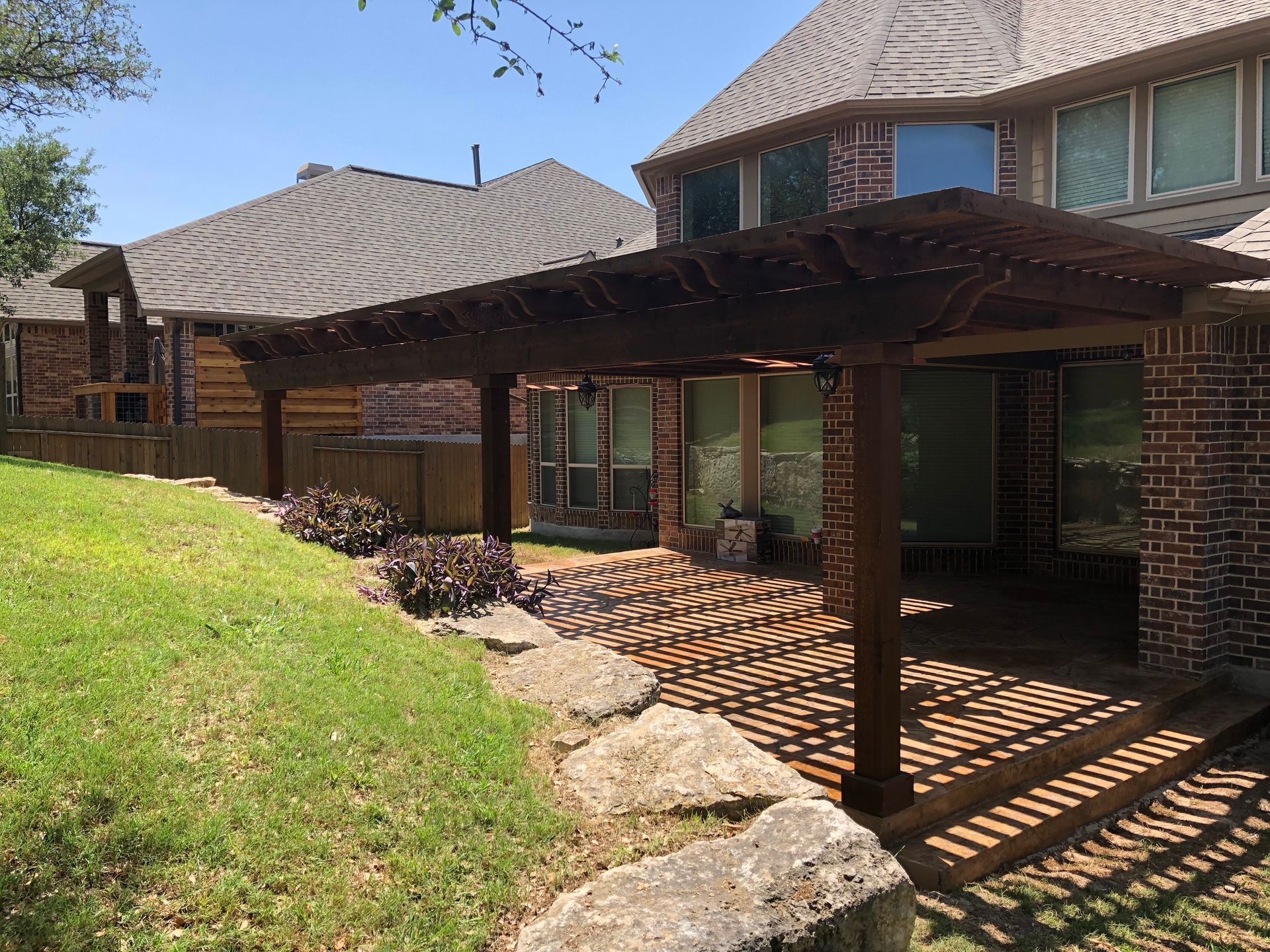 A brick house with a wooden pergola in front of it built by Fine Patio Design San Antonio TX
