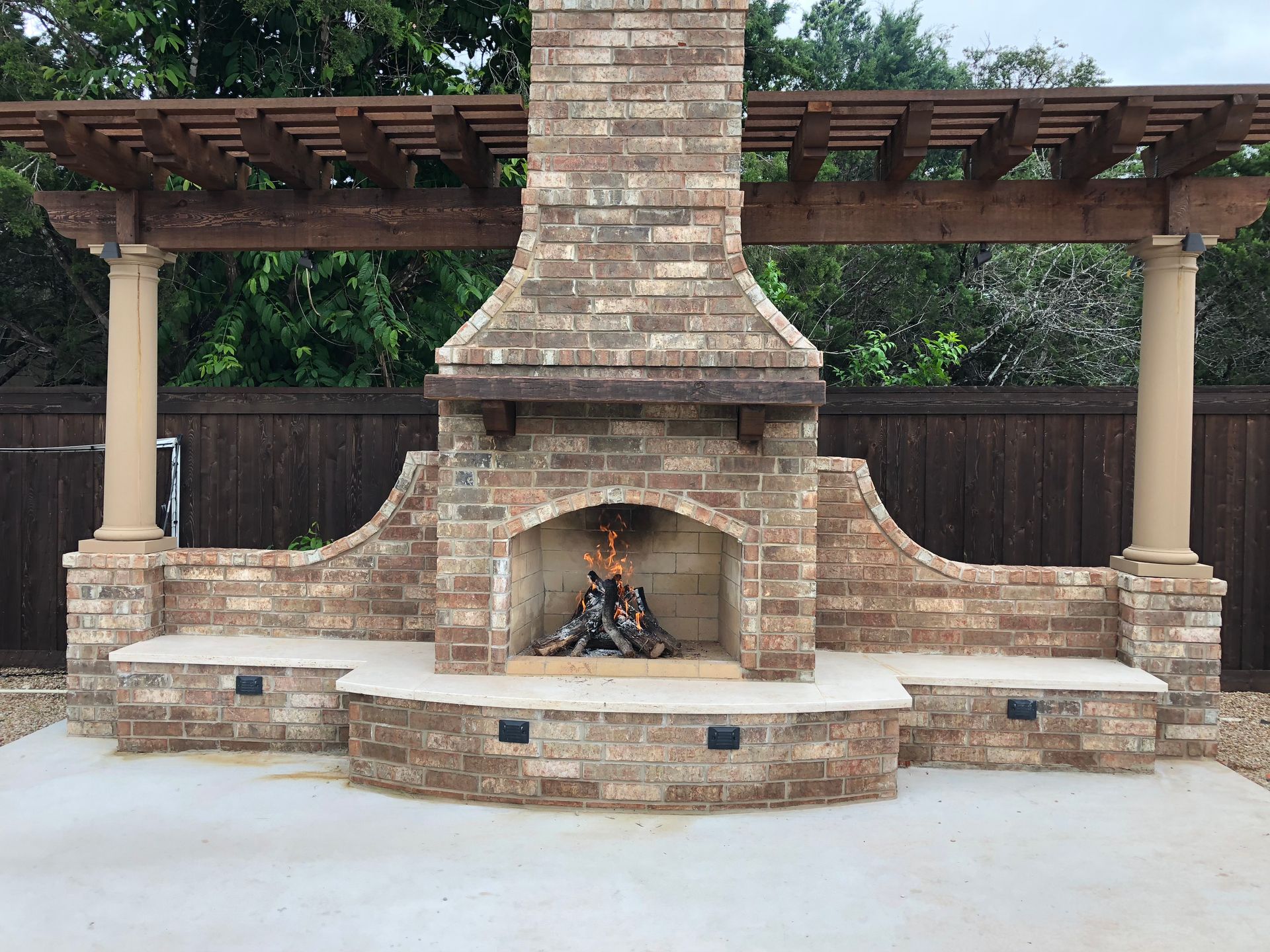 A brick fireplace with a wooden pergola over it built by Fine Patio Design San Antonio TX