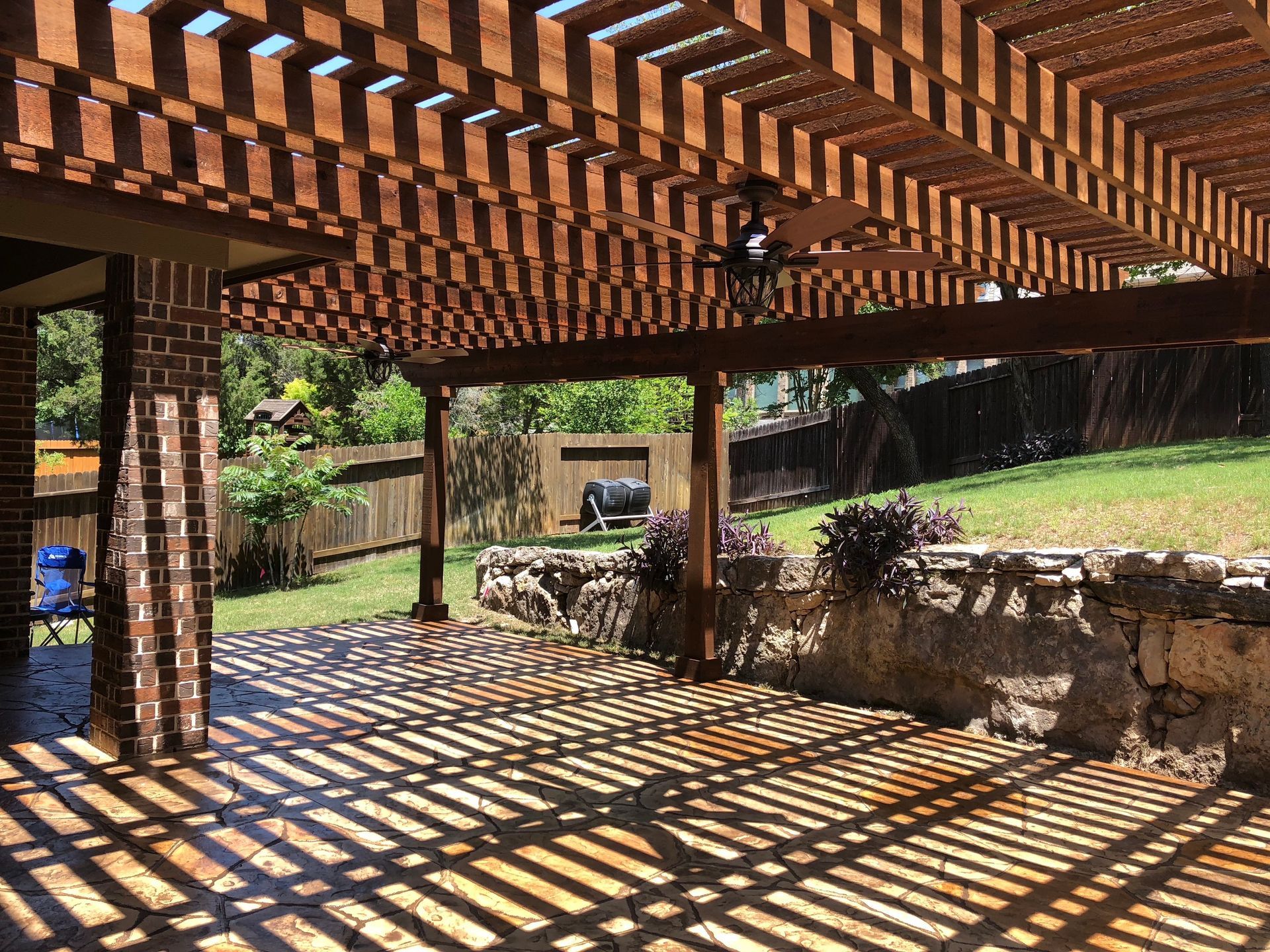 A patio with a wooden pergola and a ceiling fan built by Fine Patio Design San Antonio TX