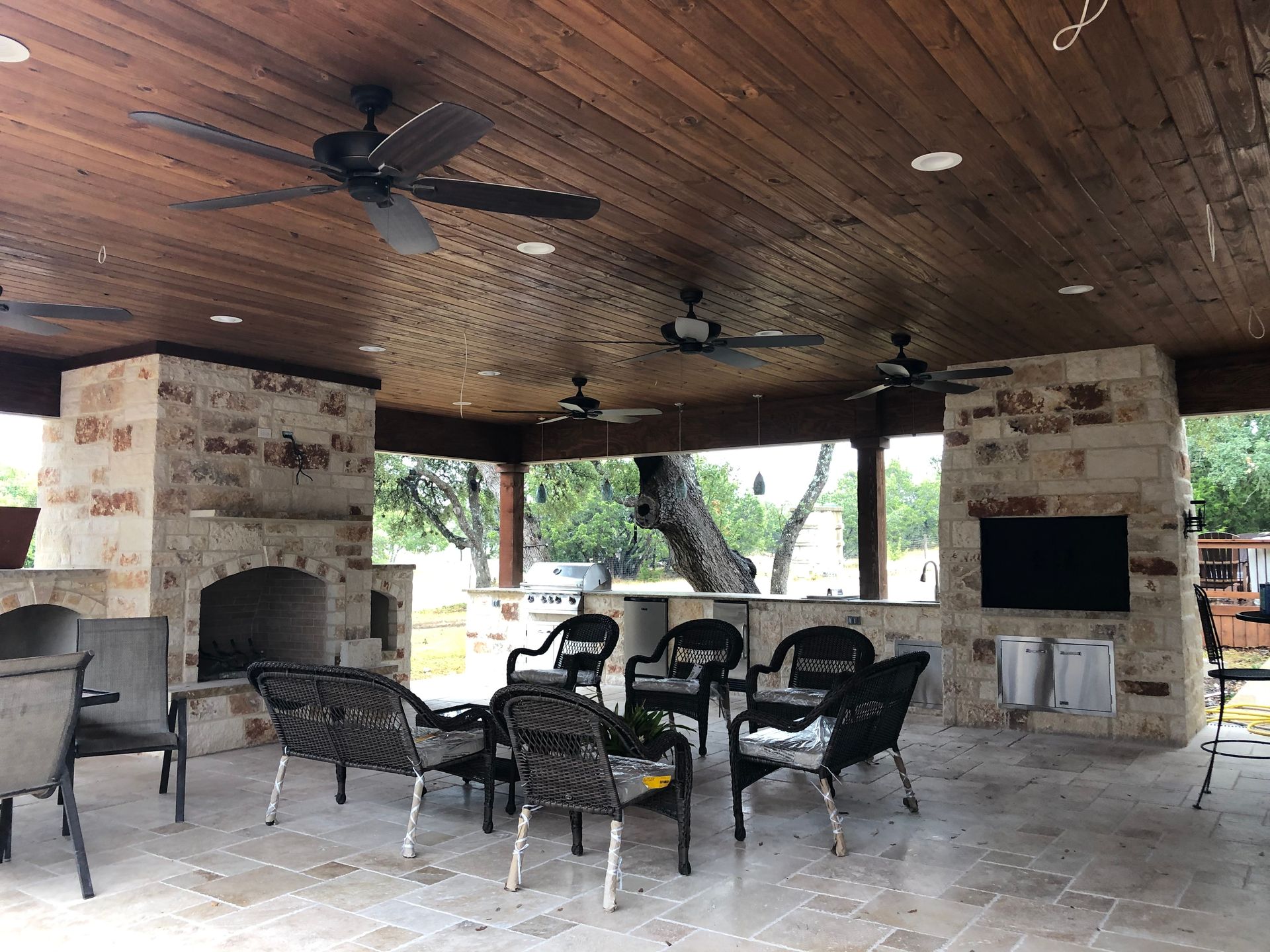 A patio area with a fireplace and ceiling fans built by Fine Patio Design San Antonio TX