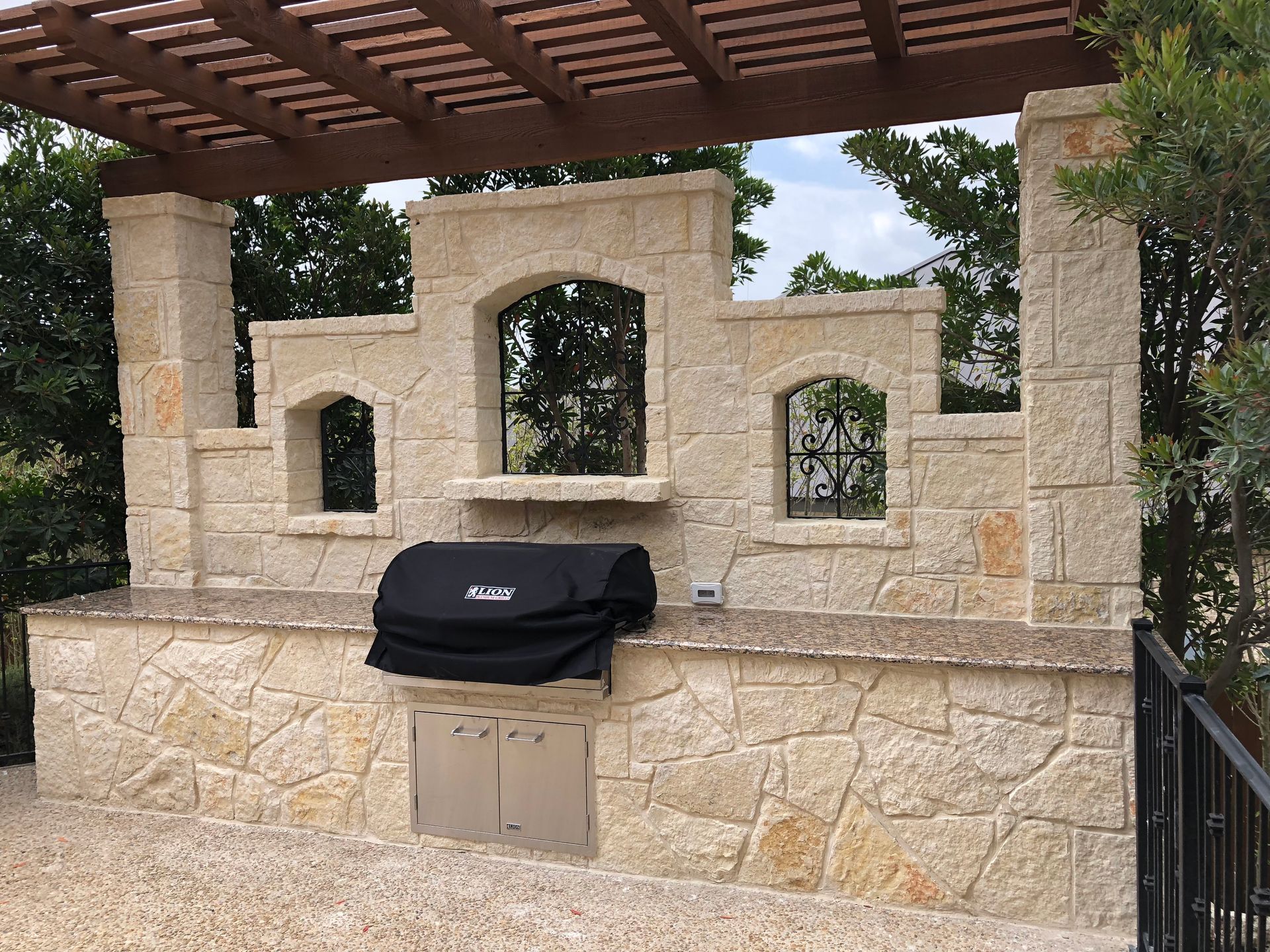 A grill with a black cover sits under a pergola built by Fine Patio Design San Antonio TX