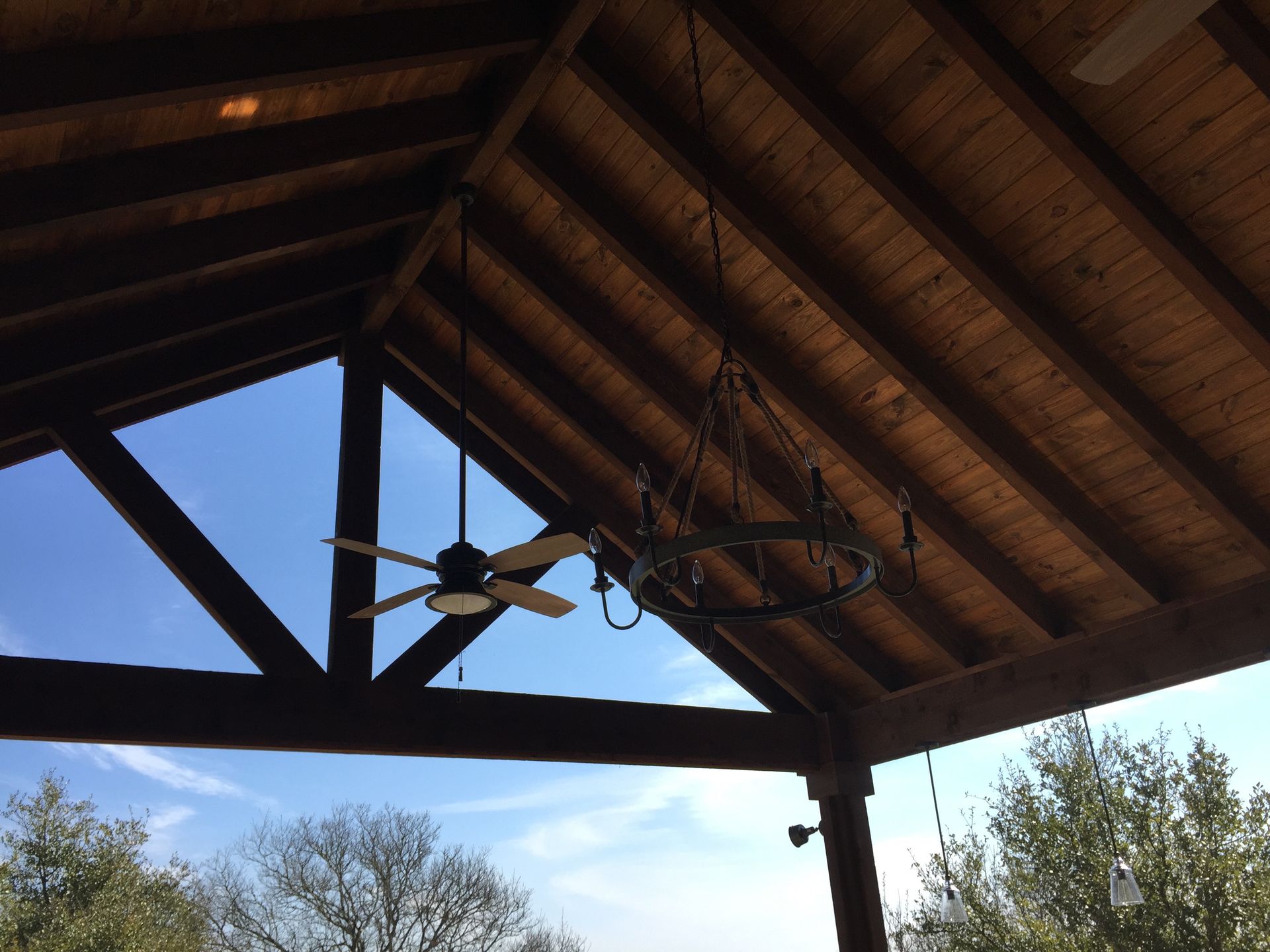 A wooden ceiling with a ceiling fan and a chandelier hanging from it built by Fine Patio Design San Antonio TX