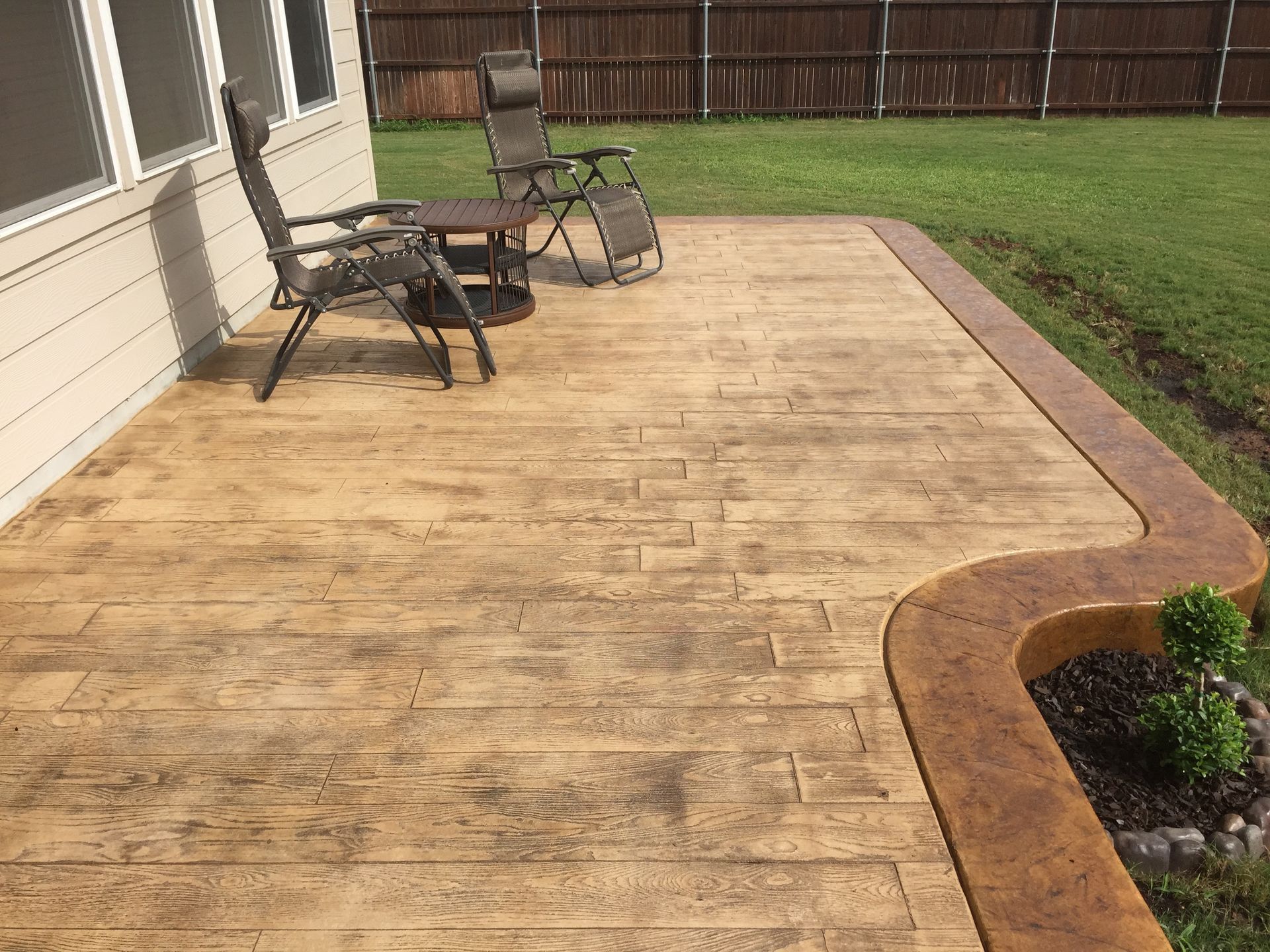 A decorative concrete patio with chairs and a table in front of a house built by Fine Patio Design San Antonio TX