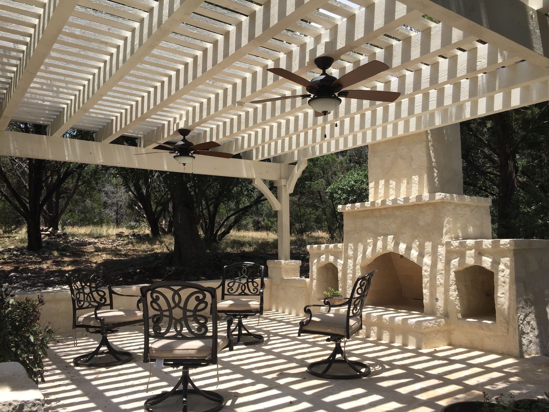A patio with chairs and a fireplace under a pergola built by Fine Patio Design San Antonio TX