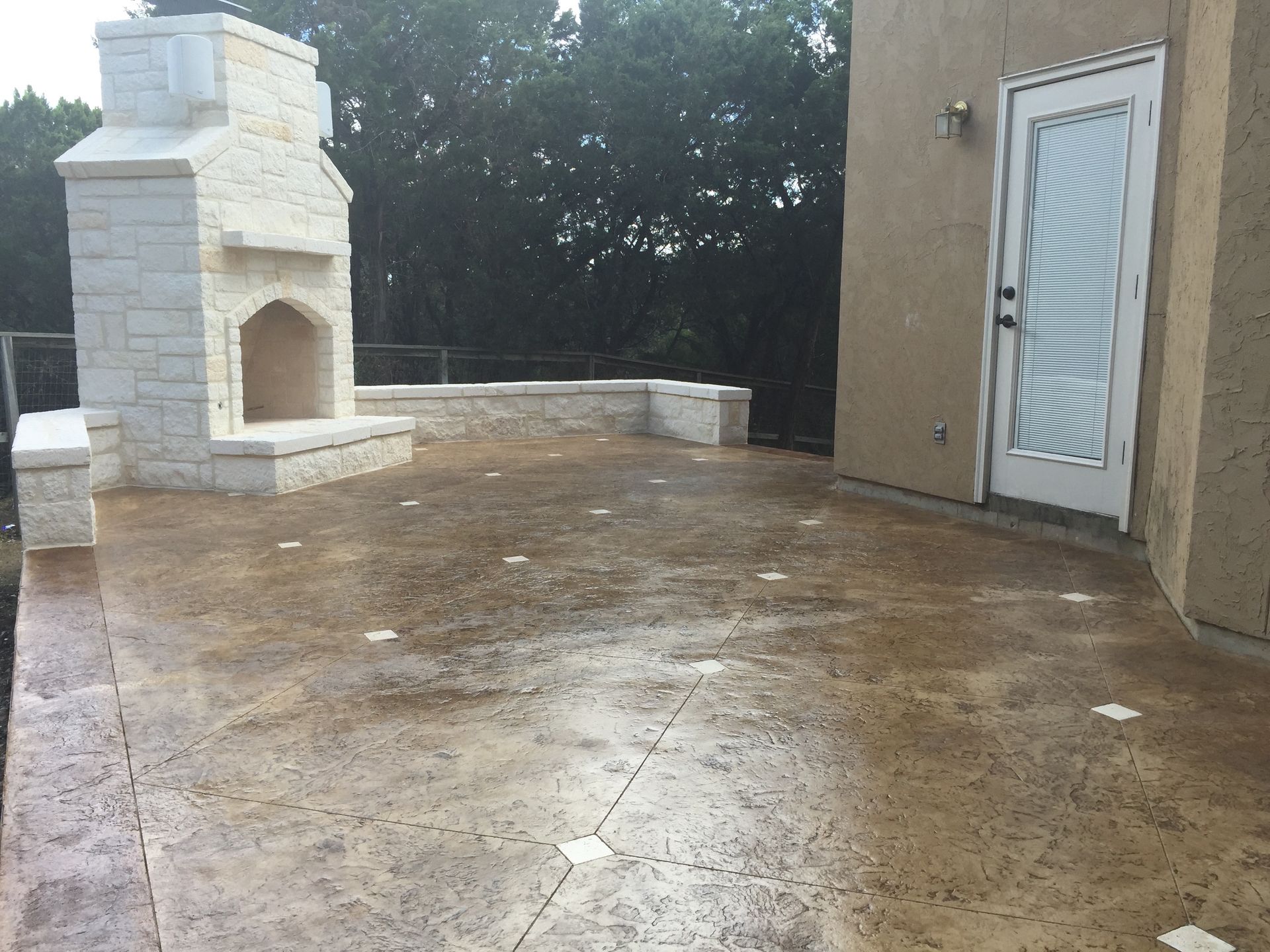 A decorative concrete patio with a fireplace and a sliding glass door built by Fine Patio Design San Antonio TX