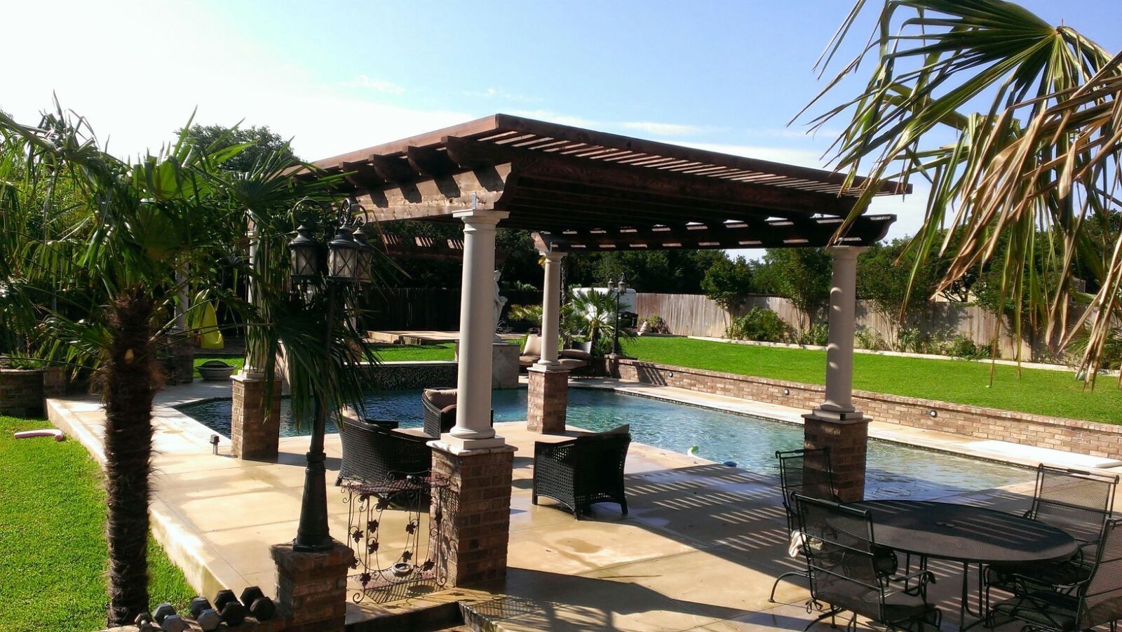 A patio area with a pergola and a swimming pool built by Fine Patio Design San Antonio TX