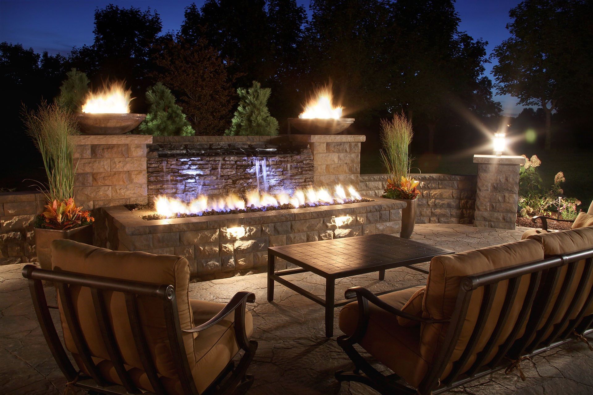 A patio with a fire pit and a waterfall at night built by Fine Patio Design San Antonio TX 