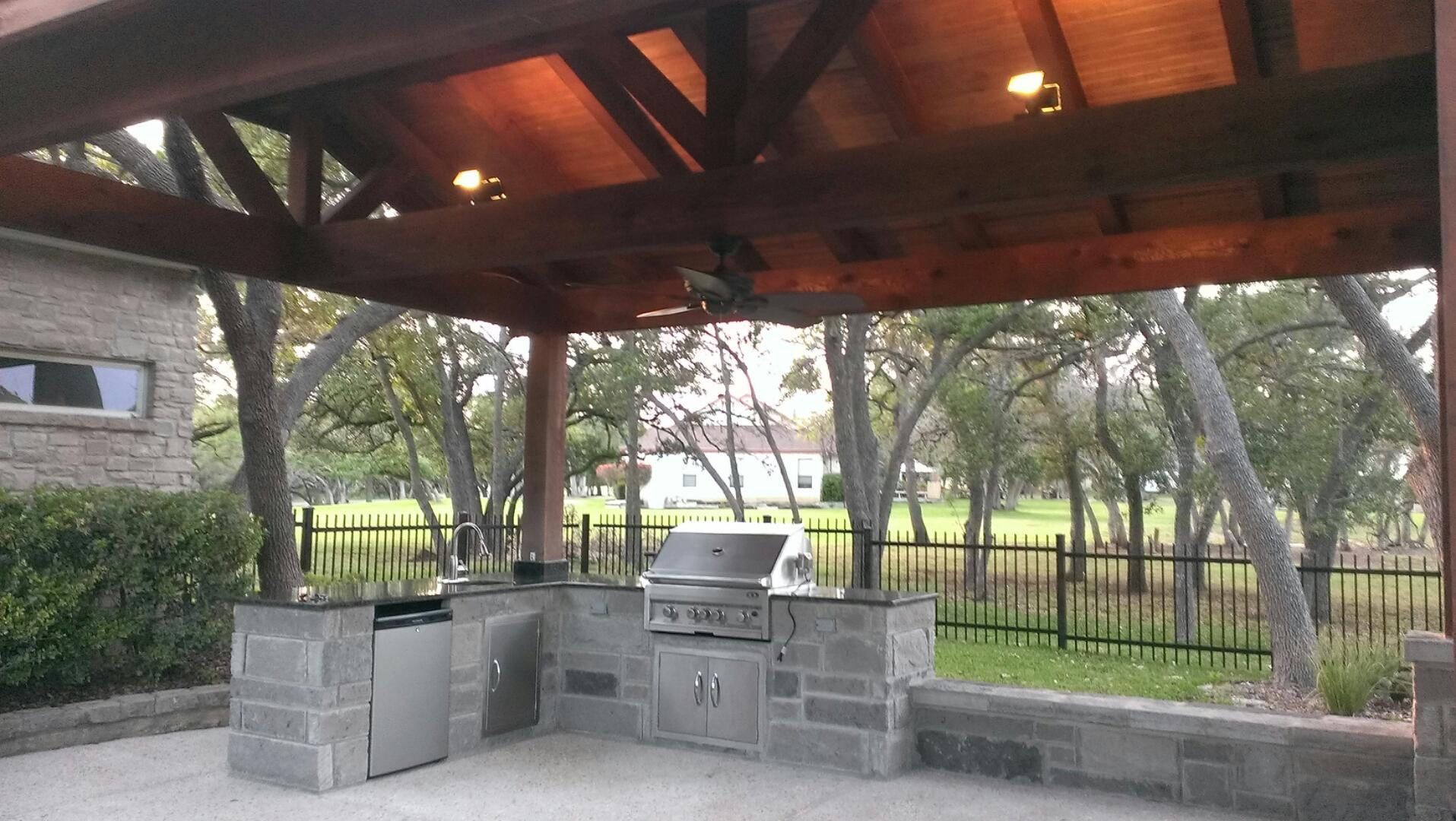 An outdoor kitchen with a grill under a wooden roof built by Fine Patio Design San Antonio TX