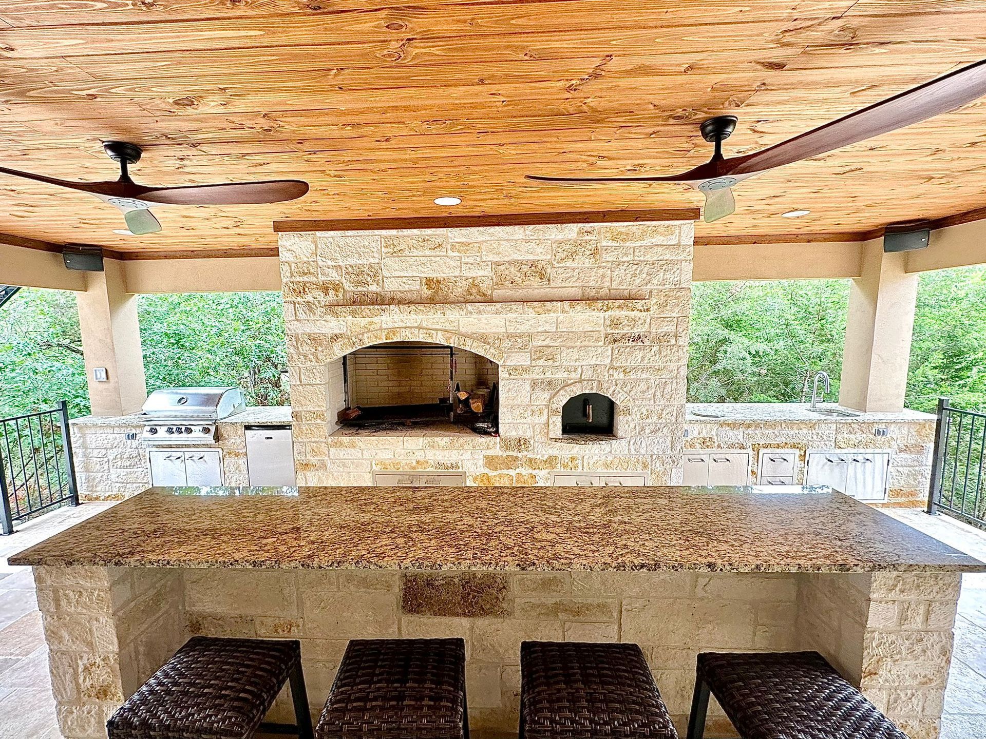 A patio area with a stone fireplace and a ceiling fan built by Fine Patio Design San Antonio TX